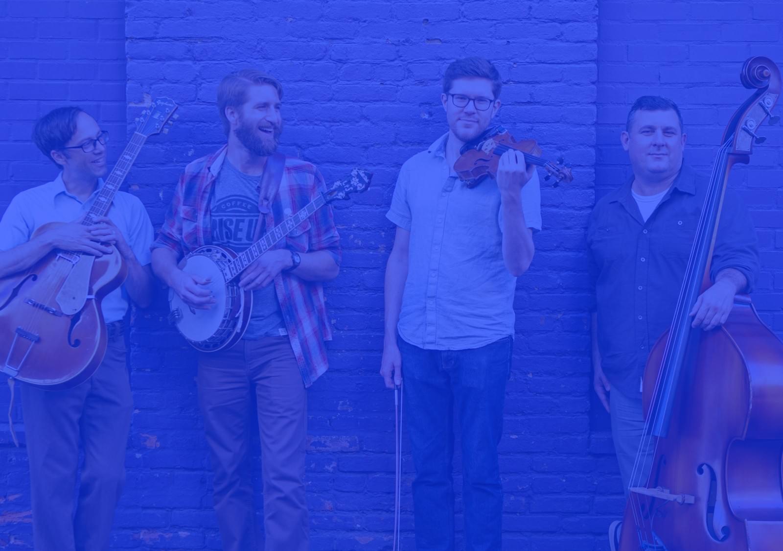 The High & Wides bluegrass band standing against a blue brick wall